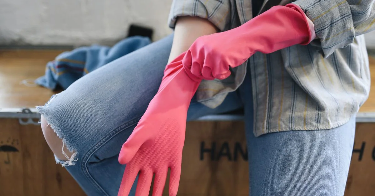 Une personne porte des gants en caoutchouc roses à l'intérieur, se préparant à des tâches de nettoyage.