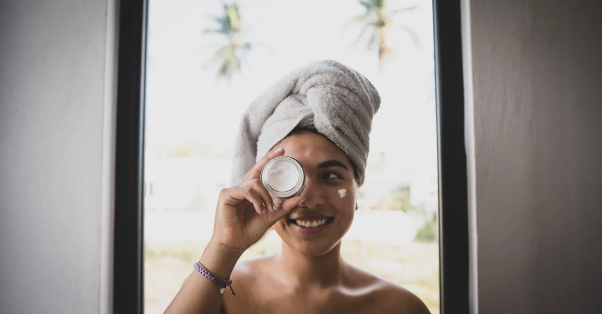 Femme souriante avec un turban en serviette et de la crème pour le visage à l'intérieur.