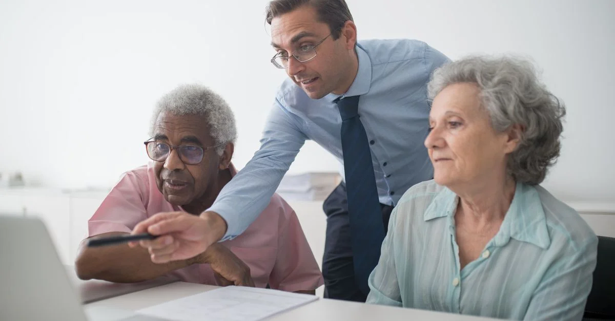 Un consultant en affaires expliquent des options financières à des clients seniors, utilisant un ordinateur portable pour illustration.