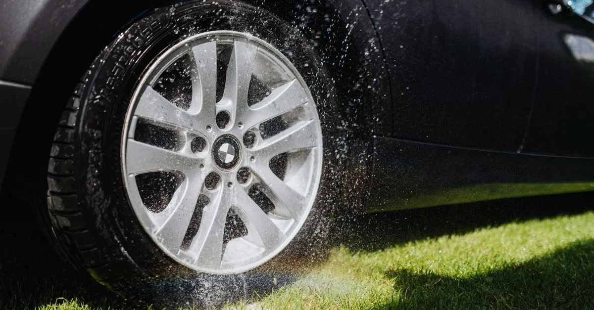 Image dynamique d'une roue de voiture arrosée pendant un lavage sur de l'herbe verte.